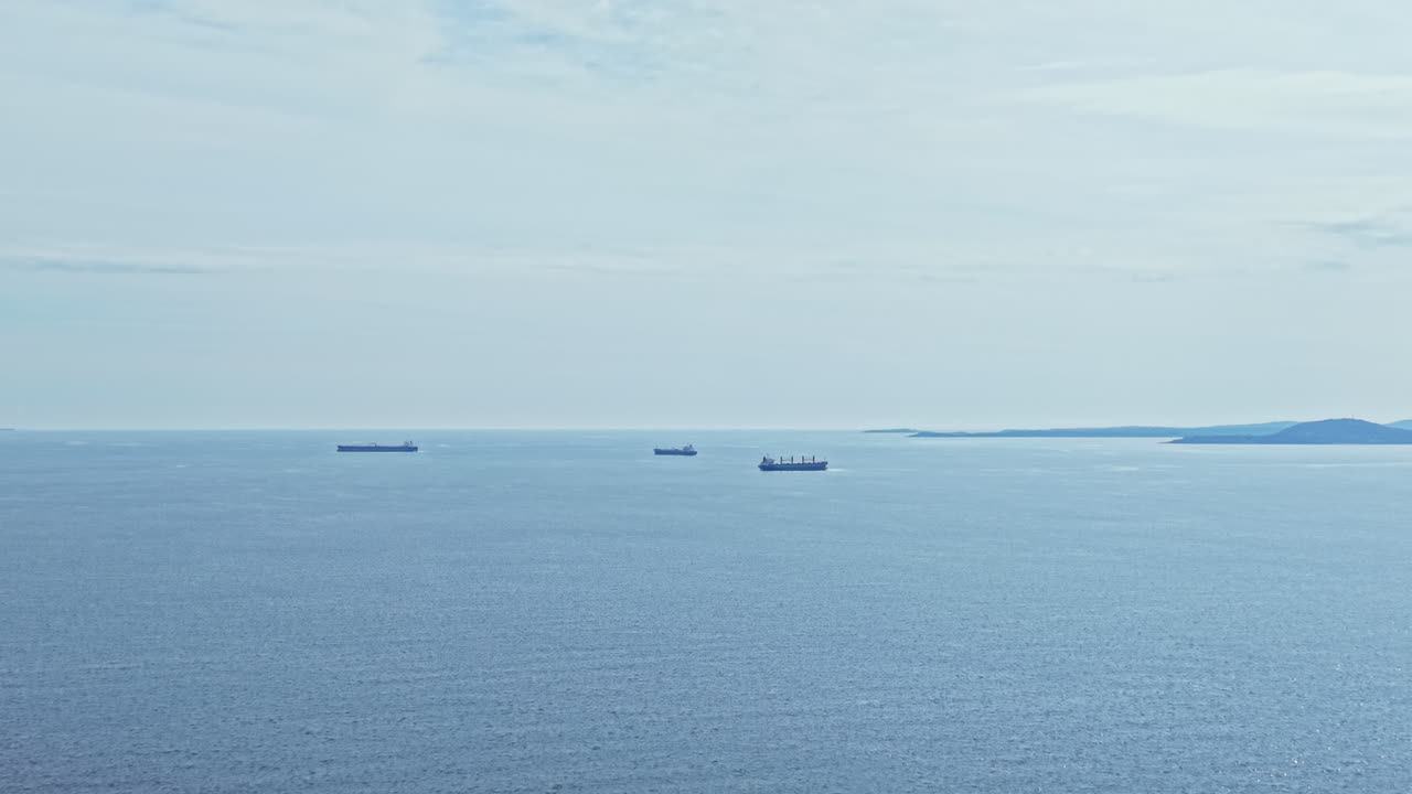 Oil tanker ships are anchored in the sea near a distant coast during daylight hours under a clear sky