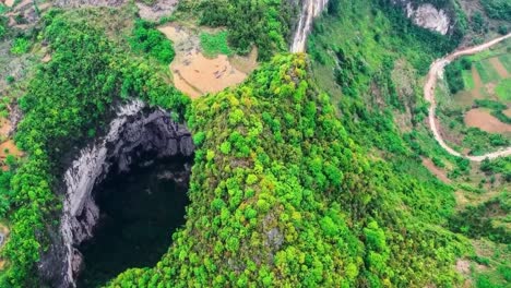 aerial drone flying over xiaozhai tiankeng heavnely pit sinkhole in a steep cliff at china during a cloudy day. sinkhole is surrounded by green nature trees and fields and steep mountains around it.