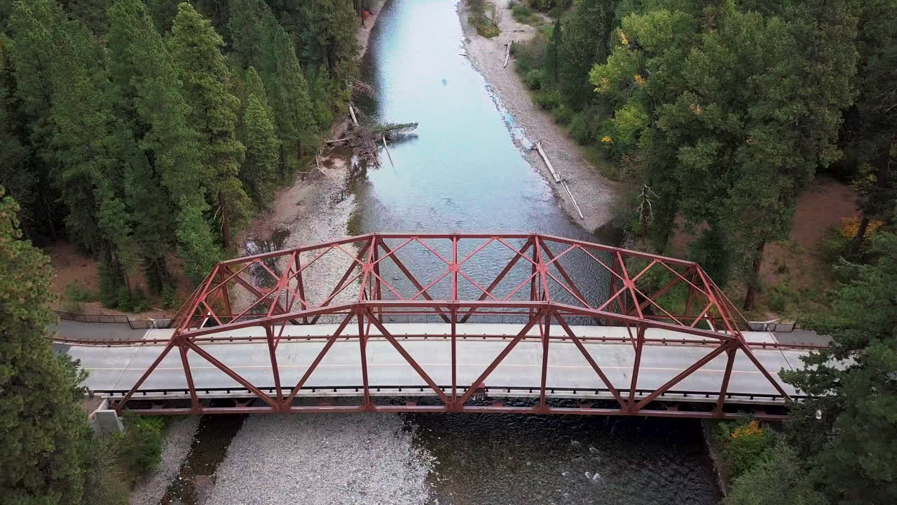 Aerial footage of a red truss bridge spanning a small river.