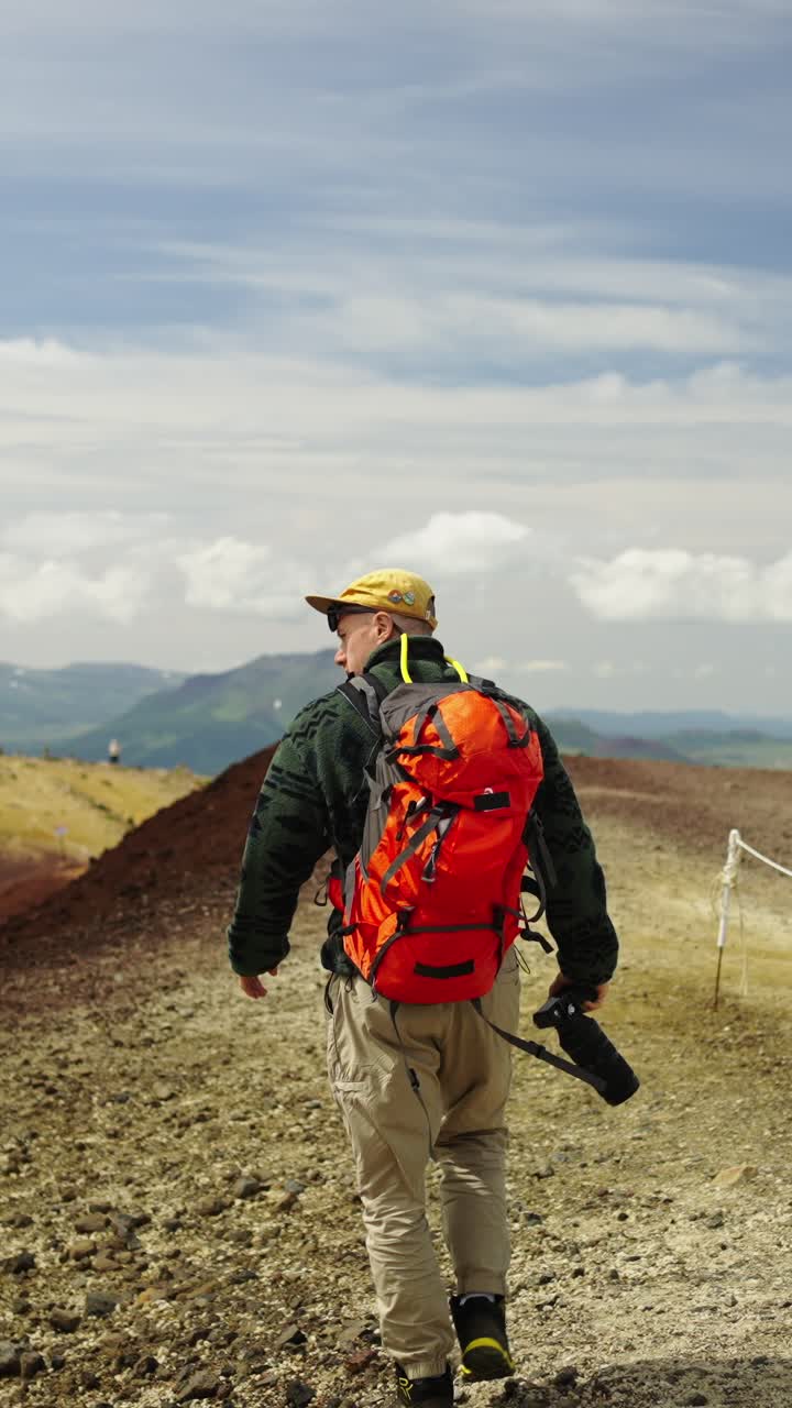 Uomo con zaino e macchina fotografica in escursione su un sentiero di montagna