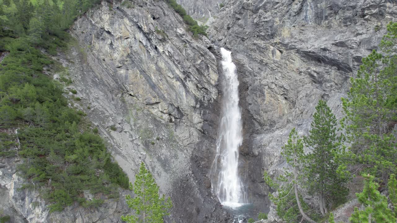 imágenes aéreas de drones que descienden lentamente hacia el dosel de un árbol mientras se enfrentan a una espectacular cascada que cae en cascada sobre el borde de un acantilado de montaña en suiza