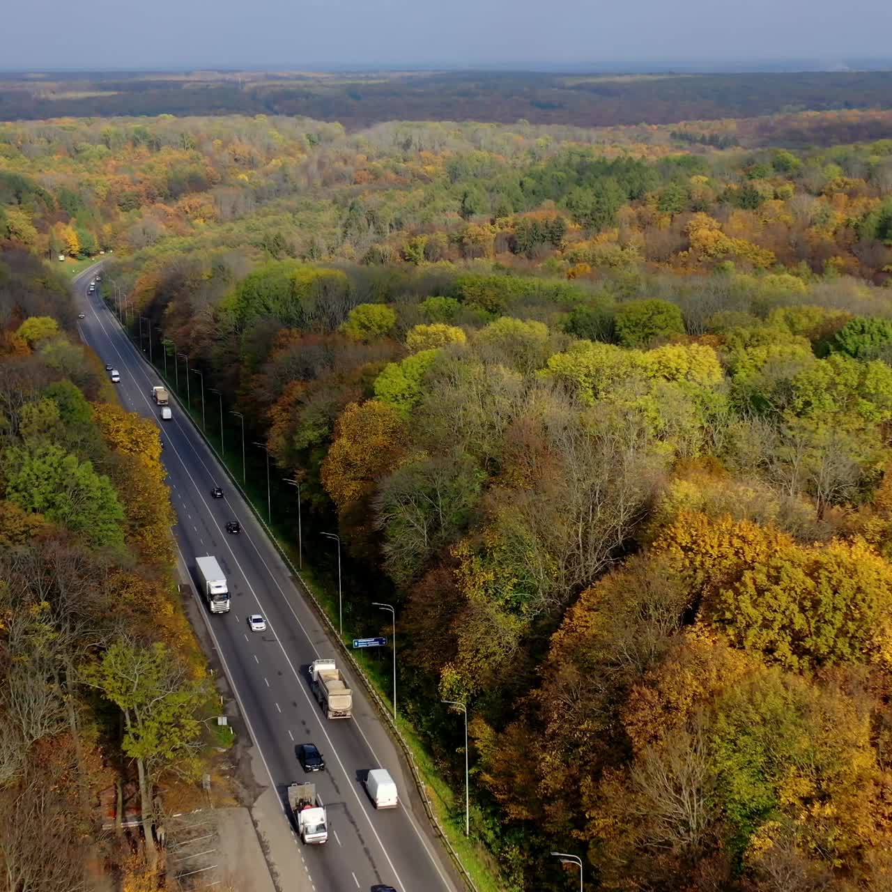Road with cars in forest. Cars driving up the road through colorful autumn forest. Colorful trees in both sides of a highway. Aerial view.