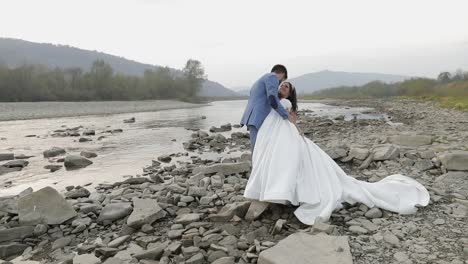 Wedding-couple-standing-near-mountain-river.-Groom-and-bride-in-love