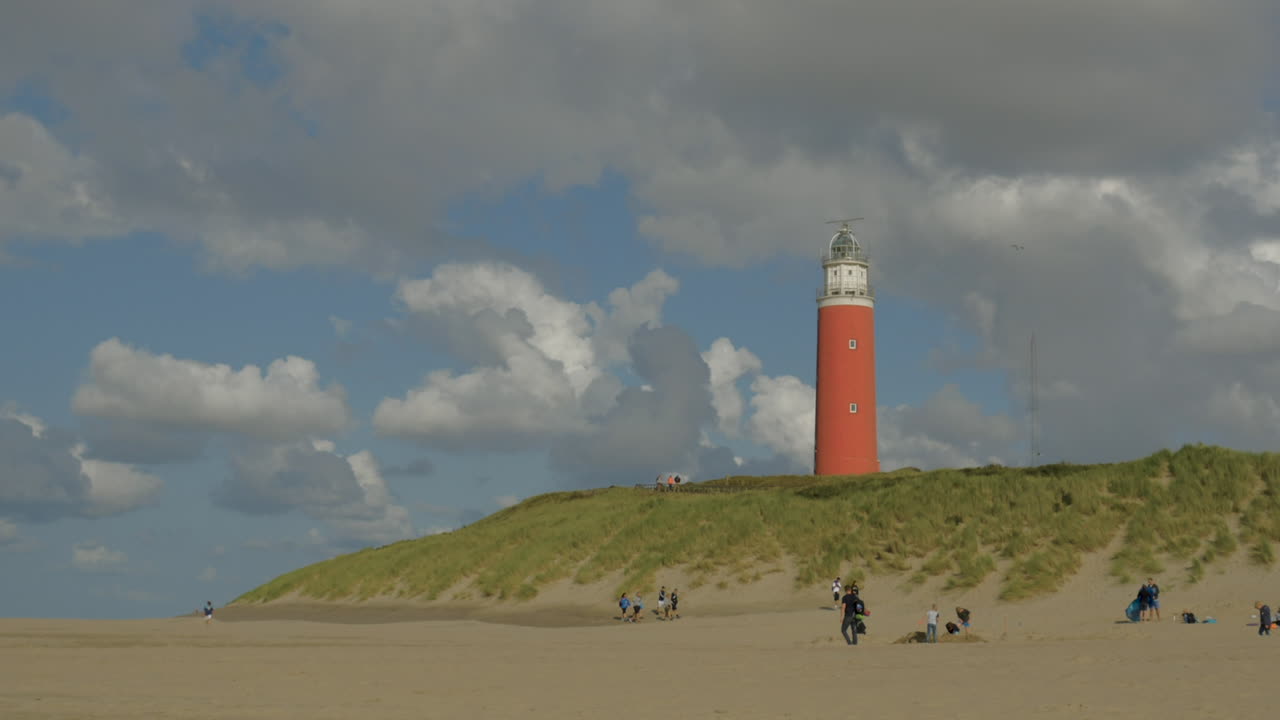 Timelapse of the Lighthouse on a Dune on Texel during summer on a half sunny day with passing clouds, people walking on the beach and on the dune next tot the lighthouse