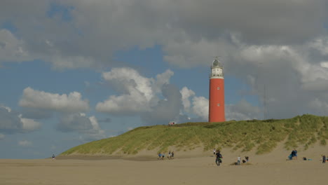 timelapse of the lighthouse on a dune on texel during summer on a half sunny day with passing clouds, people walking on the beach and on the dune next tot the lighthouse