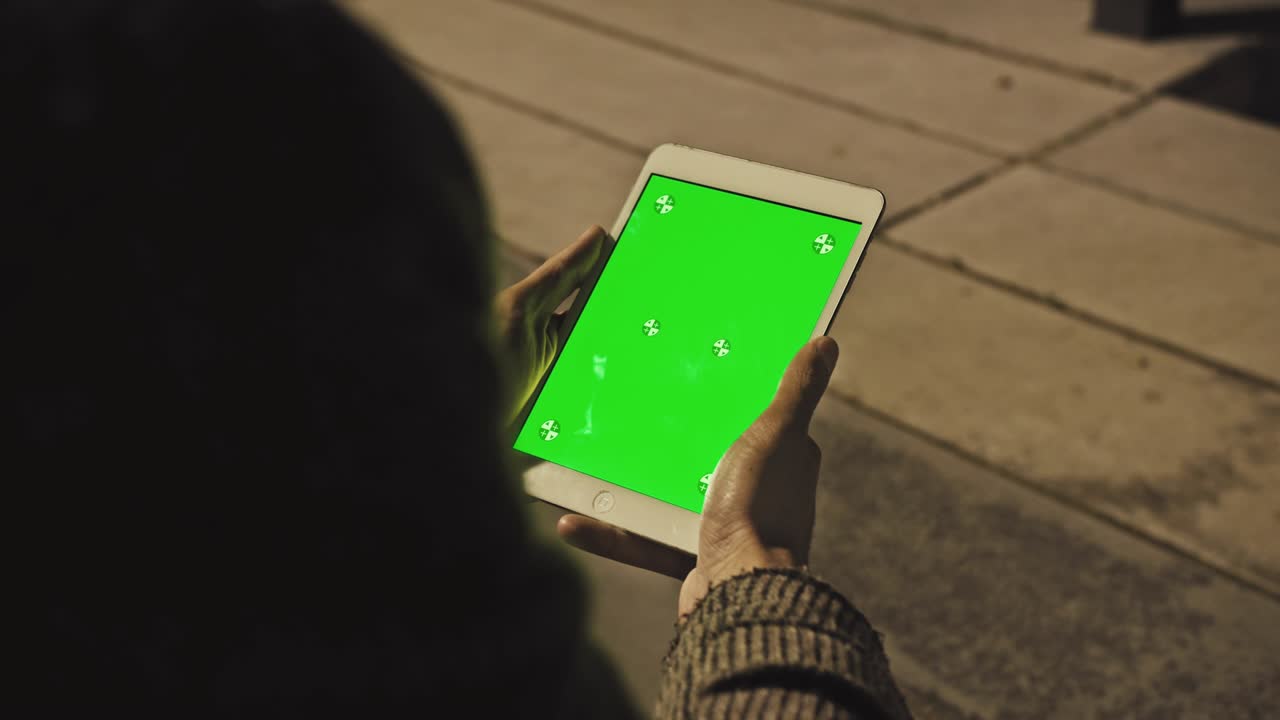 vista por encima del hombro joven en casa sentado en una silla usando con pantalla de maqueta verde tableta computadora en modo vertical. hombre usando dispositivo de pantalla táctil, navegando por internet, viendo contenido