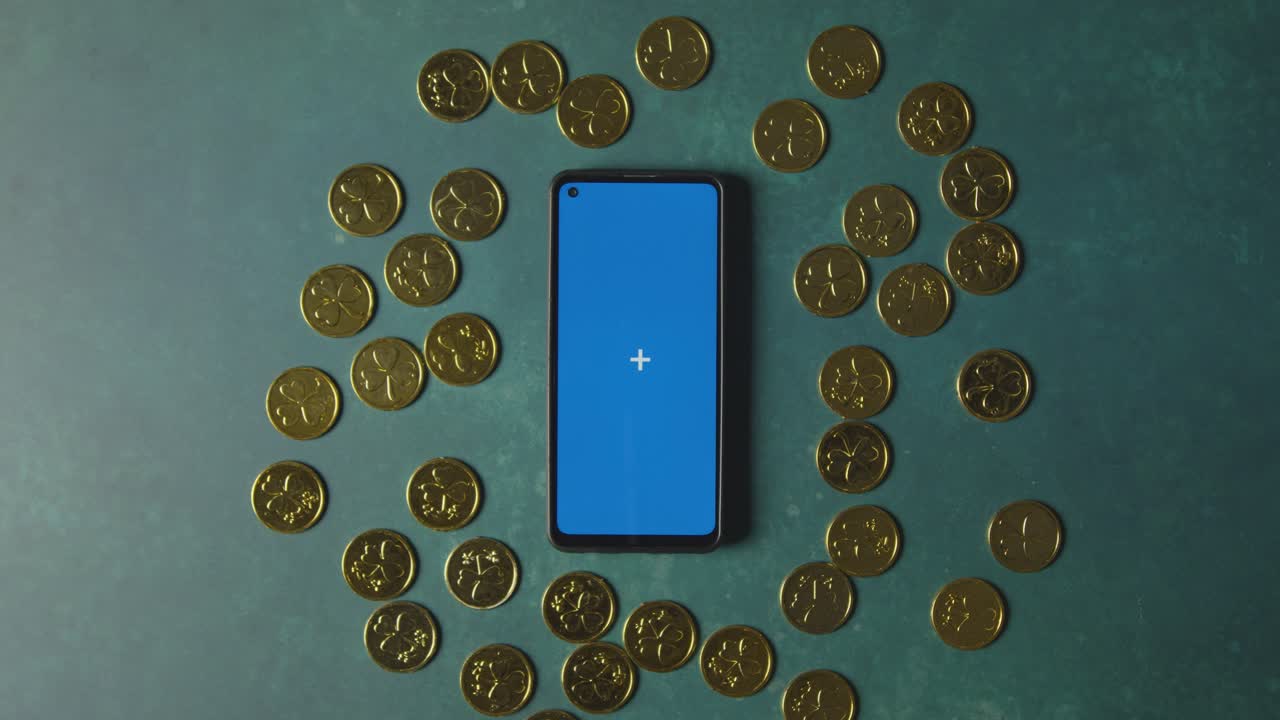 성 패트릭의 날을 축하하기 위해 블루 스크린 휴대폰을 둘러싼 금화의 오버헤드 스튜디오 샷