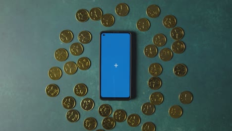 foto de estudio superior de monedas de oro que rodean el teléfono móvil de pantalla azul para celebrar el día de san patricio