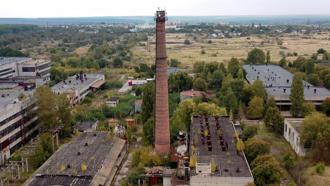 Old factory buildings in the countryside. Large brick pipe on abandoned plant. Large territory with destroyed warehouses. Aerial view.