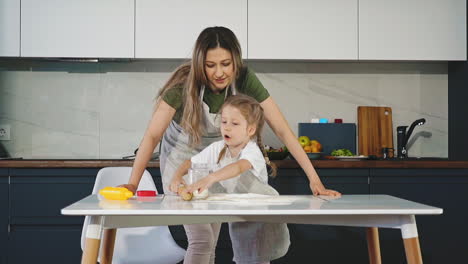 daughter-pours-flour-and-rolls-dough-with-mother-at-table