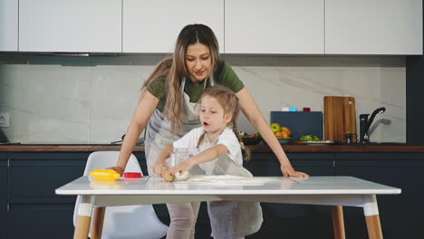 daughter pours flour and rolls dough with mother at table