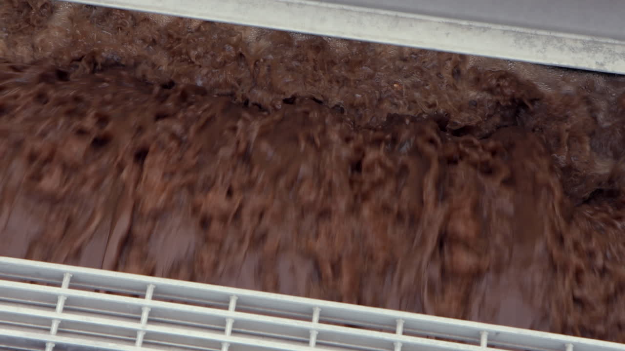 Cascading brown wastewater churns turbulently through an aeration process at a treatment plant, capturing industrial flow, froth, and dynamic water movement in motion