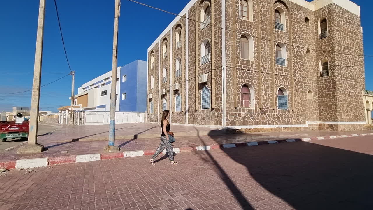 Girl with long hair walks on a lonely street in Casa del mar, Tarfaya,, Marroco. 4K videos. camera following girl walking