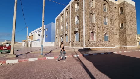 girl with long hair walks on a lonely street in casa del mar, tarfaya,, marroco. 4k videos. camera following girl walking
