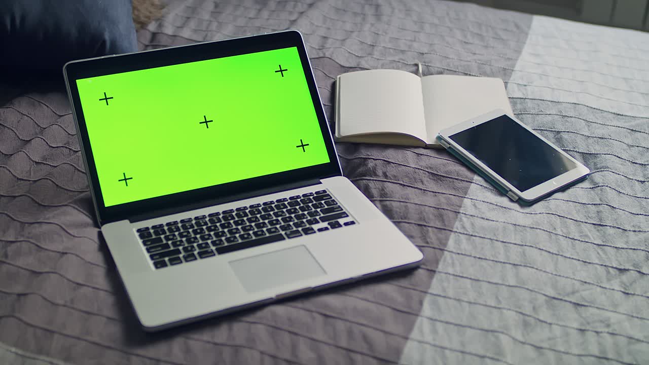 The laptop, notebook with green screen and tracking markers. Mobile tablet lying on the bedspread.