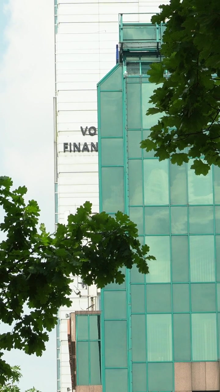 Una vista cinematografica dell'architettura contemporanea a Varsavia, Polonia, con facciate in vetro ed edifici del quartiere finanziario incorniciati da una lussureggiante vegetazione estiva.