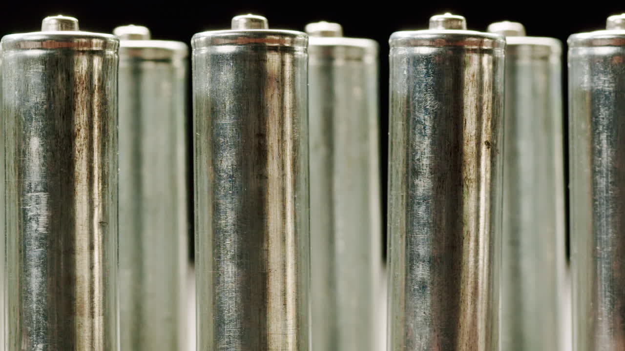 Silver batteries AA and AAA on black background close-up. Double-A battery is a standard size single cell cylindrical dry battery. Batteries are common in portable electronic devices. An AA battery is composed of a single electrochemical cell that may be either a primary battery or a rechargeable ba