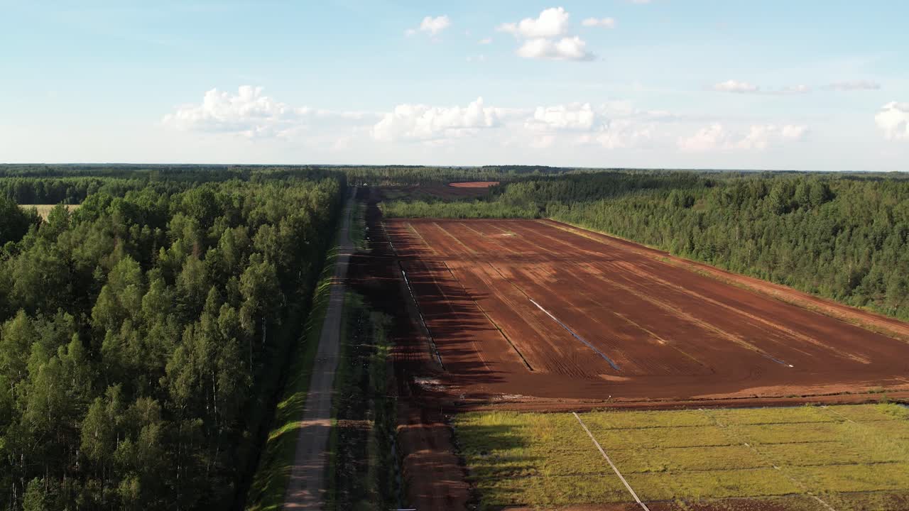 Aerial view of a large peat bog harvesting site with long parallel rows of extracted peat, wooden pallets, and covered stacks stretching across the landscape