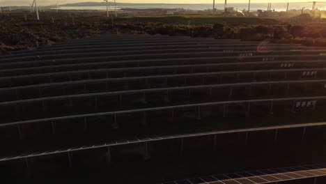 Scenic-aerial-of-solar-panel-farm-with-wind-turbines-and-chimneys-on-background