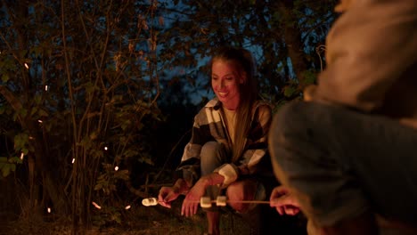 pov: a girl and a boy are roasting marshmallows on a bonfire and tasting them. a party outside the city. rest in the country house