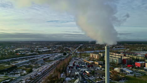 Small township with industrial factory emitting smoke from chimney, aerial fly through smoke