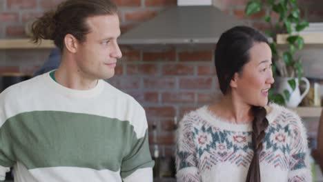 Three-happy-diverse-female-and-male-friends-talking-while-cooking-together-in-kitchen