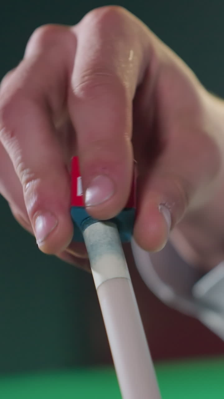 백색 셔츠를 입은 손이 조심스럽게 크레이드를 키우 스틱에 적용하는 클로즈업, 뒷면에 흐릿한 녹색 테이블과 함께 빨간색과 파란색 크레이드에 초점을 맞추고, 정확성을 강조합니다.