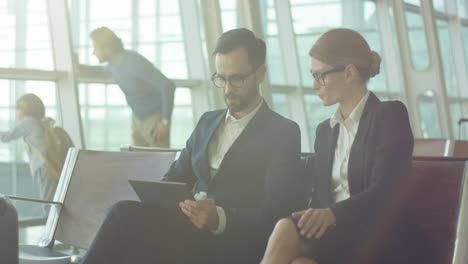 atractivo hombre de negocios y mujer de negocios sentado en el aeropuerto y trabajando en el dispositivo de tableta mientras espera un vuelo