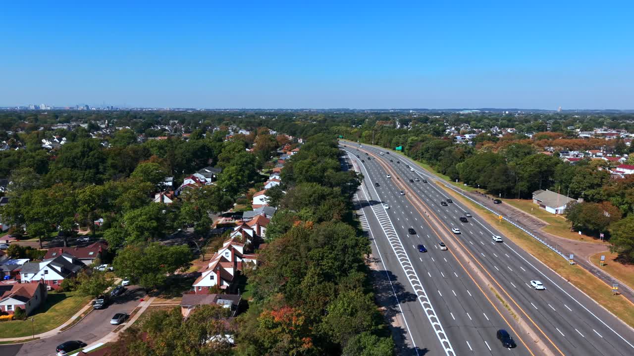 Aerial view of the Southern State Parkway on Long Island, NY during a sunny day with light automobile traffic. The camera dolly in and boom down over the green trees beside the parkway