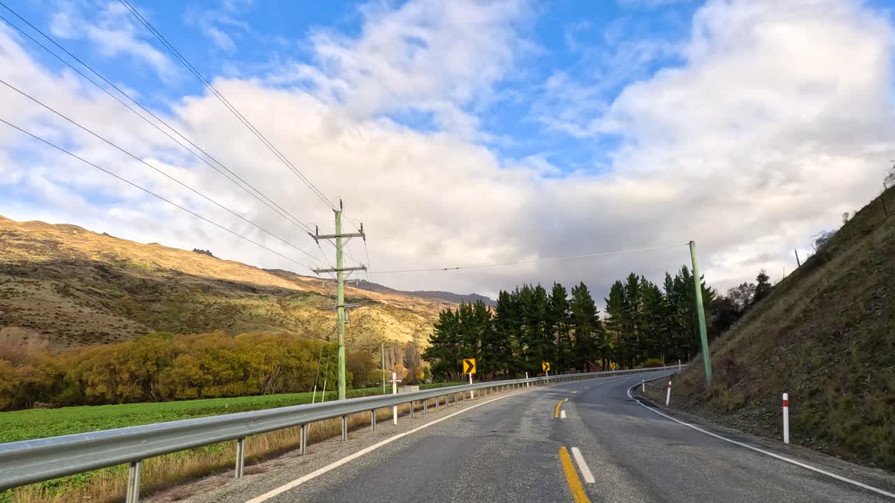 A tranquil drive along a winding road in Wanaka, New Zealand, showcasing lush greenery and expansive skies under soft daylight