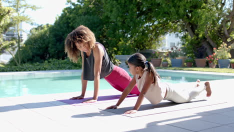 happy biracial mother and daughter practicing yoga pose in sunny garden, slow motion