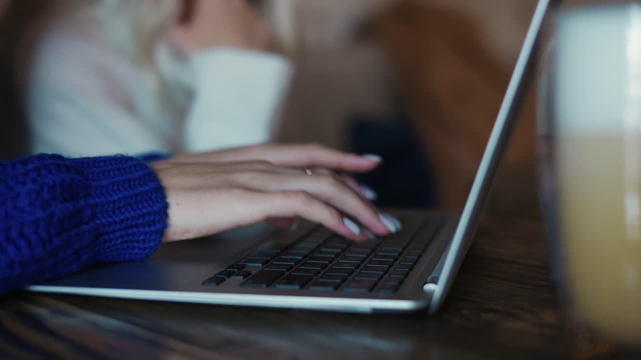 Female freelancer's hands with manicure typing on laptop keyboard in cafe