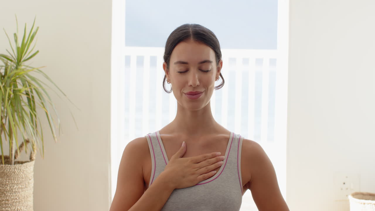 Woman practicing mindfulness with hand on chest, eyes closed, feeling peaceful, at home