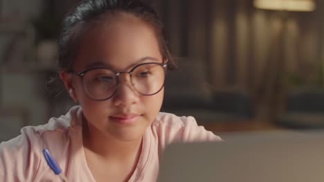 close up teenage girl learning online from laptop at night