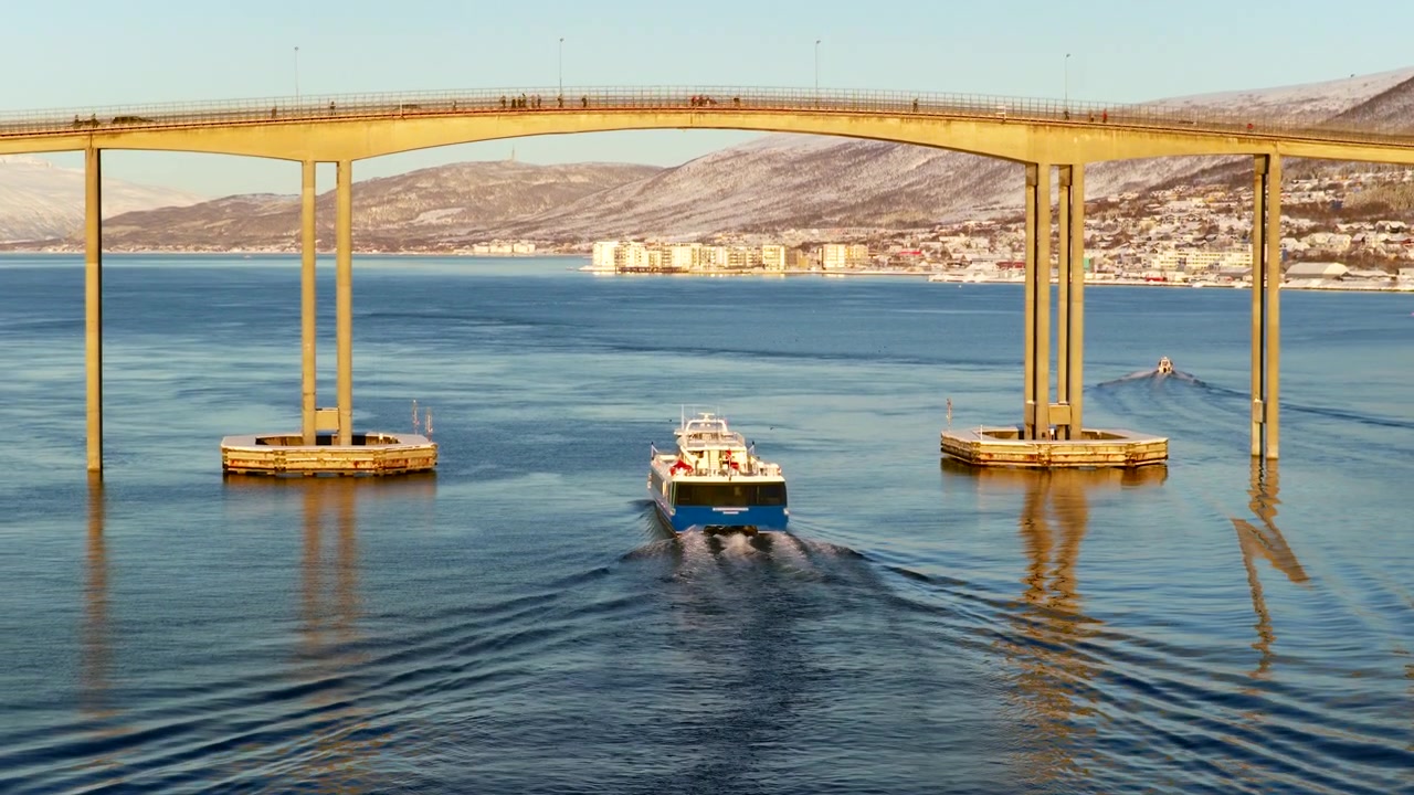 Barco de ecoturismo navegando sob a ponte da cidade de Tromso em um passeio de fiorde de inverno. Aéreo.