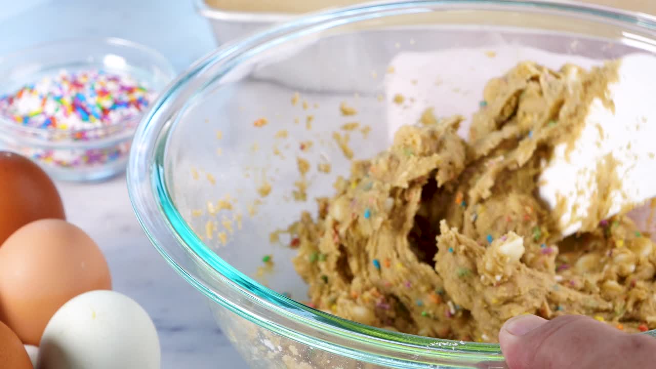Baking confetti sugar cookies and using a spatula to mix the batter. Making cookies and placing the batter on a sheet with a spoon to bake.. In the kitchen making confetti sugar cookies with sprinkle