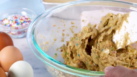 baking confetti sugar cookies and using a spatula to mix the batter. making cookies and placing the batter on a sheet with a spoon to bake.. in the kitchen making confetti sugar cookies with sprinkle