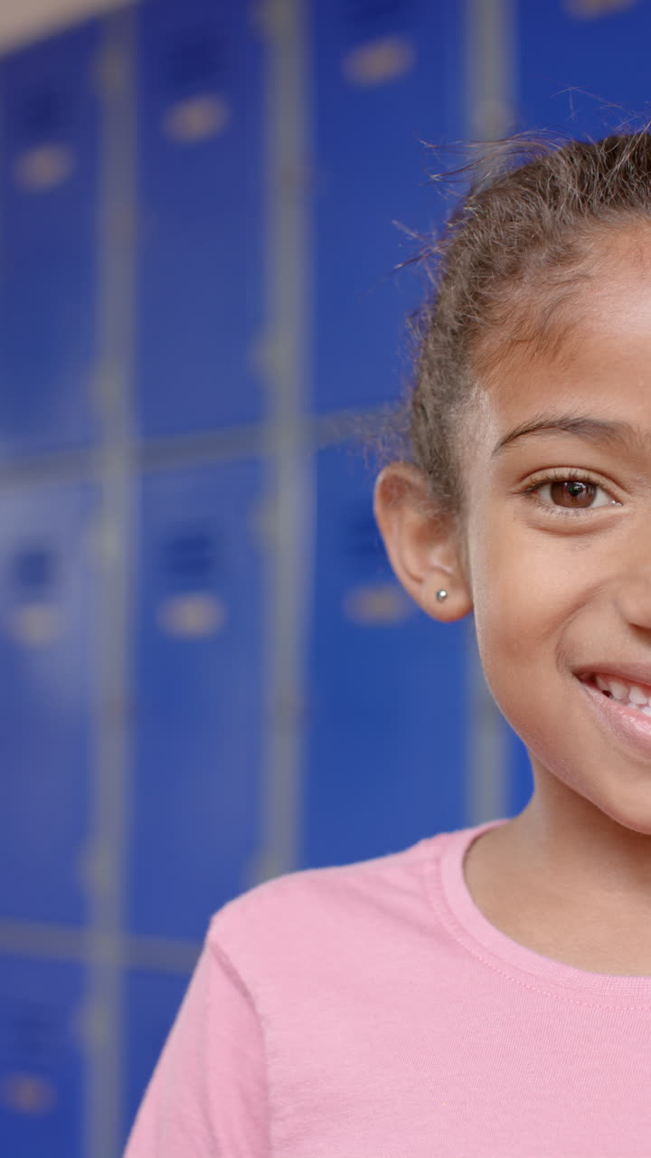 Vertical video: In school, young biracial female student stands smiling, blue background