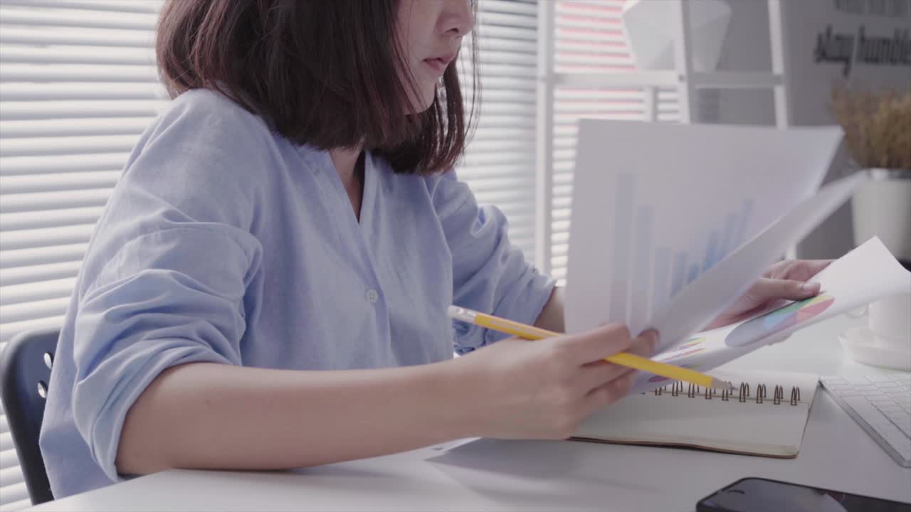 Beautiful young strain asian woman working on laptop while sitting in a living room at home. Asian business woman working in her home office.