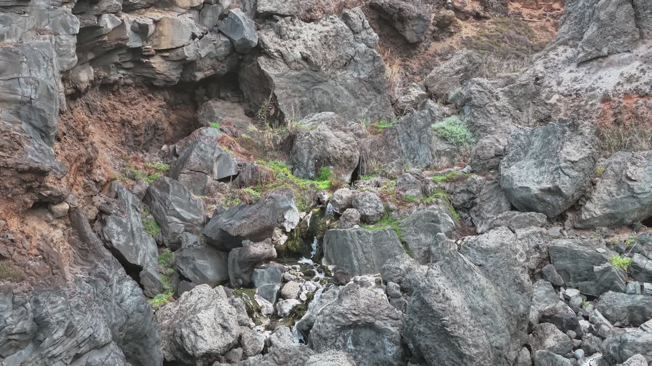 A small waterfall flows over dark volcanic rocks in Tenerife, showcasing natural island beauty