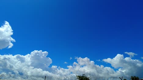 Lapso-De-Tiempo-De-Hermosas-Nubes-De-Algodón-Sobre-Una-Cerca-De-Alambre-De-Púas-Durante-El-Día-Soleado-En-Jambur,-Gambia,-áfrica-Occidental