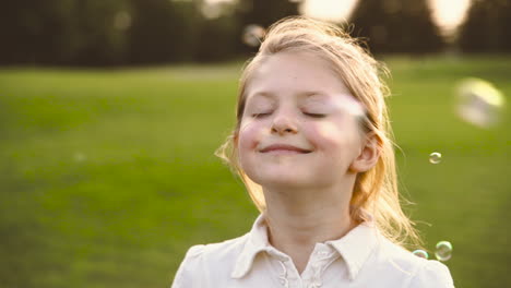 ritratto di una bambina bionda carina con gli occhi chiusi che ride circondata da bolle di sapone nel parco