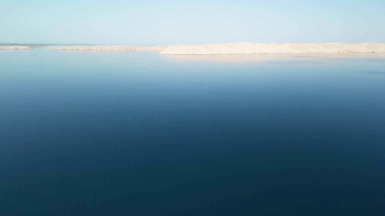una antena sobre un mar azul tranquilo con una delgada línea de tierra blanca en el sol de la mañana
