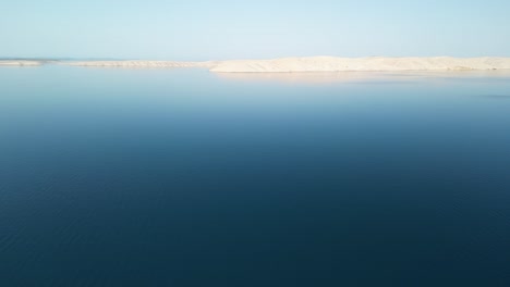 An-aerial-over-calm-blue-sea-with-thin-line-of-white-land-in-morning-sun