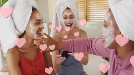 animación de corazones rosados flotando sobre felices amigas diversas que aplican máscaras faciales de belleza
