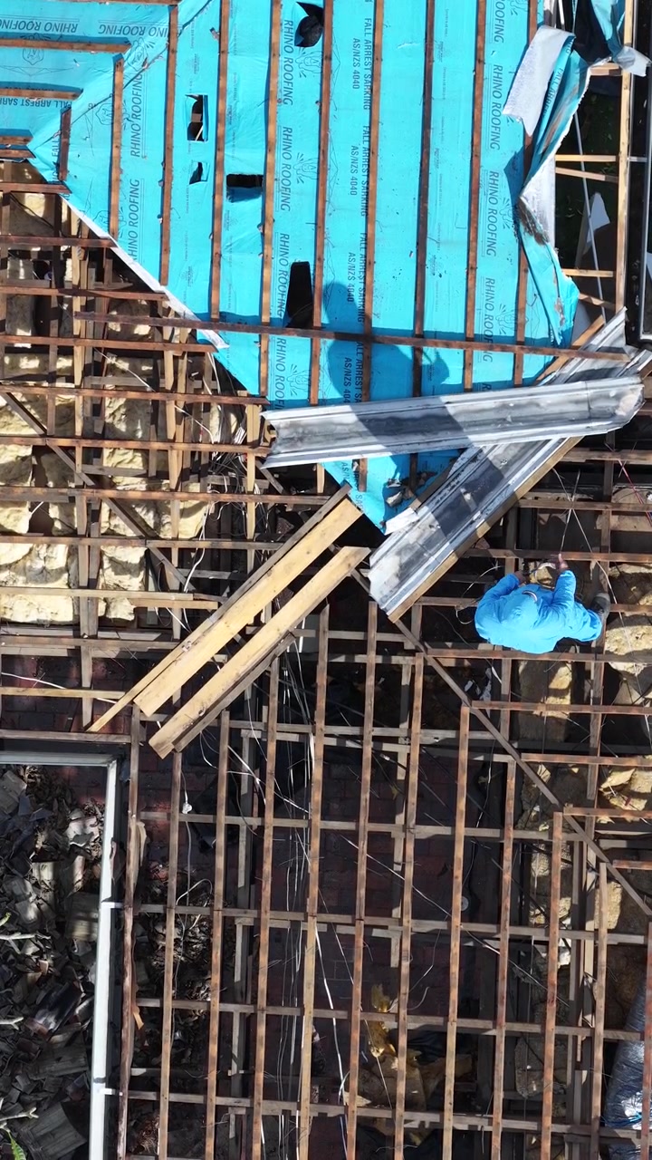 Top-down drone shot of a specialist removing hazardous materials from a residential roof structure.