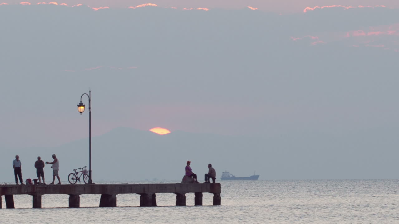 People relaxing on a pier at sunset Ship is passing by