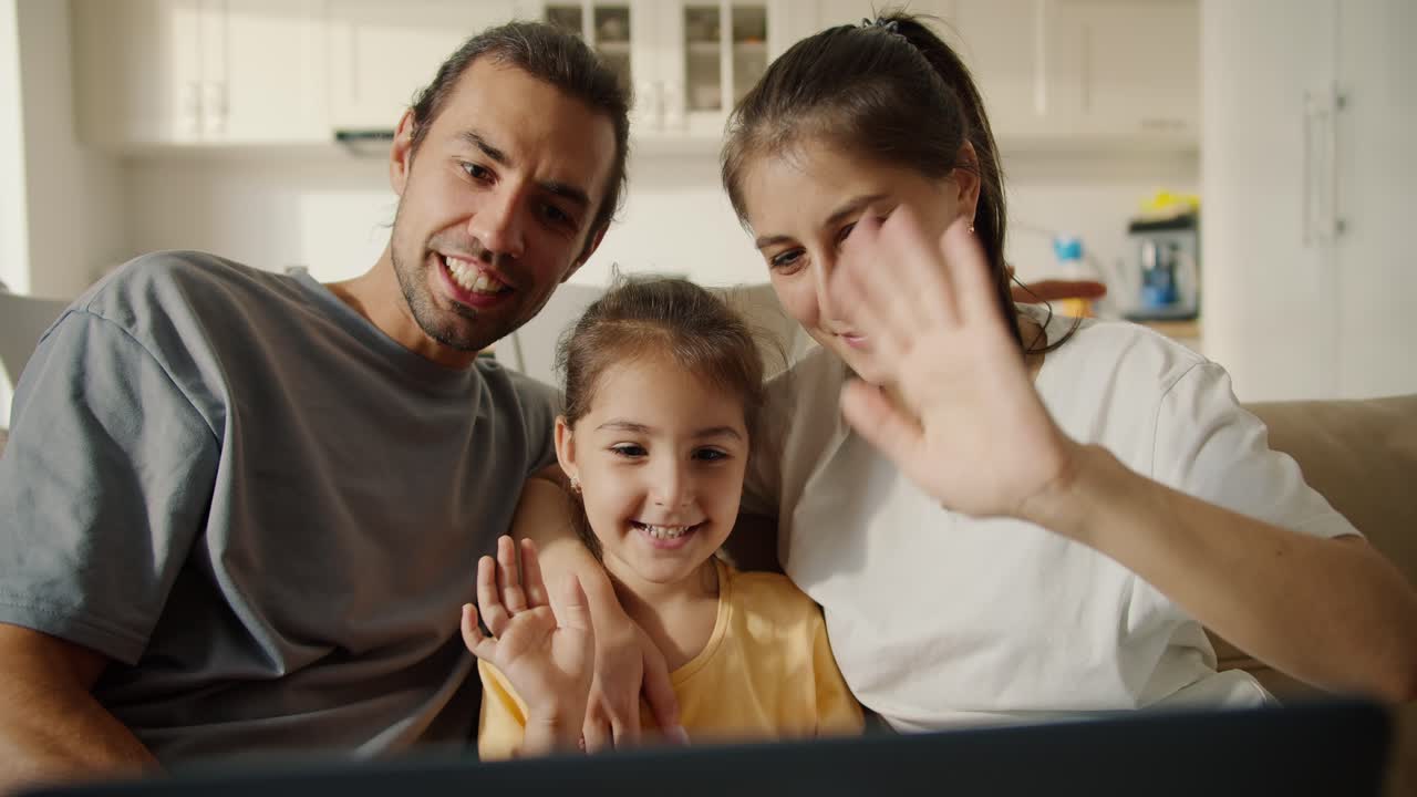 familia feliz, un chico moreno con rastro, su novia morena en una camiseta blanca y su hija alegre en un vestido amarillo se comunican con su familia y amigos a través de videoconferencia usando una computadora portátil en una sala de estudio moderna