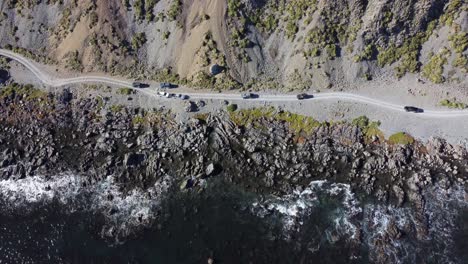 una vista de pájaro de un grupo de vehículos todoterreno que circulan por una carretera costera de grava