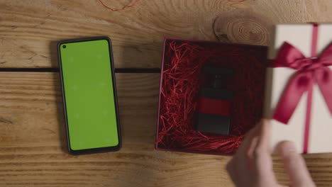 overhead shot of romantic valentines present of perfume gift wrapped in box next to green screen mobile phone